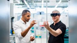 Un technicien portant des lunettes de réalité augmentée dans une usine interagissant avec un collègue.
