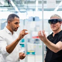 Un technicien portant des lunettes de réalité augmentée dans une usine interagissant avec un collègue.