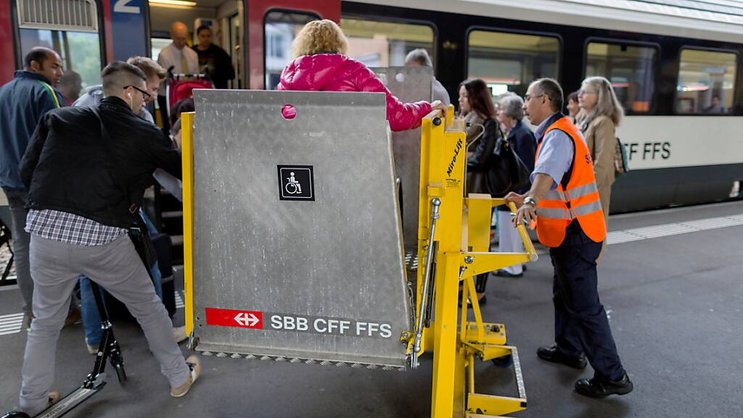 Un employé des CFF, à l'aide d'un élévateur, permet à une femme en chaise roulante d'accéder à un train.