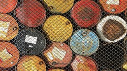 Barils de pétrole derrière une clôture grillagée.