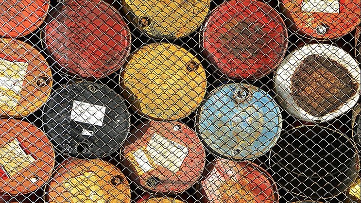 Barils de pétrole derrière une clôture grillagée.