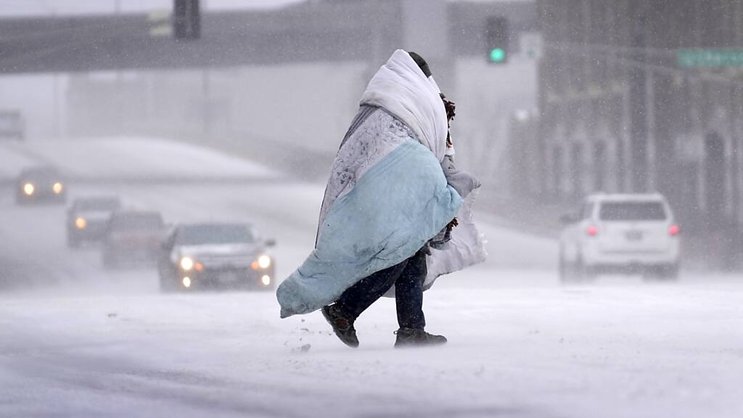 Une personne enveloppée dans une couverture traverse une rue couverte de neige à St. Louis, dans le MIssouri.