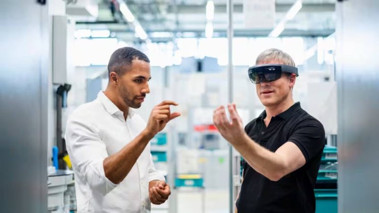 Un technicien portant des lunettes de réalité augmentée dans une usine interagissant avec un collègue.